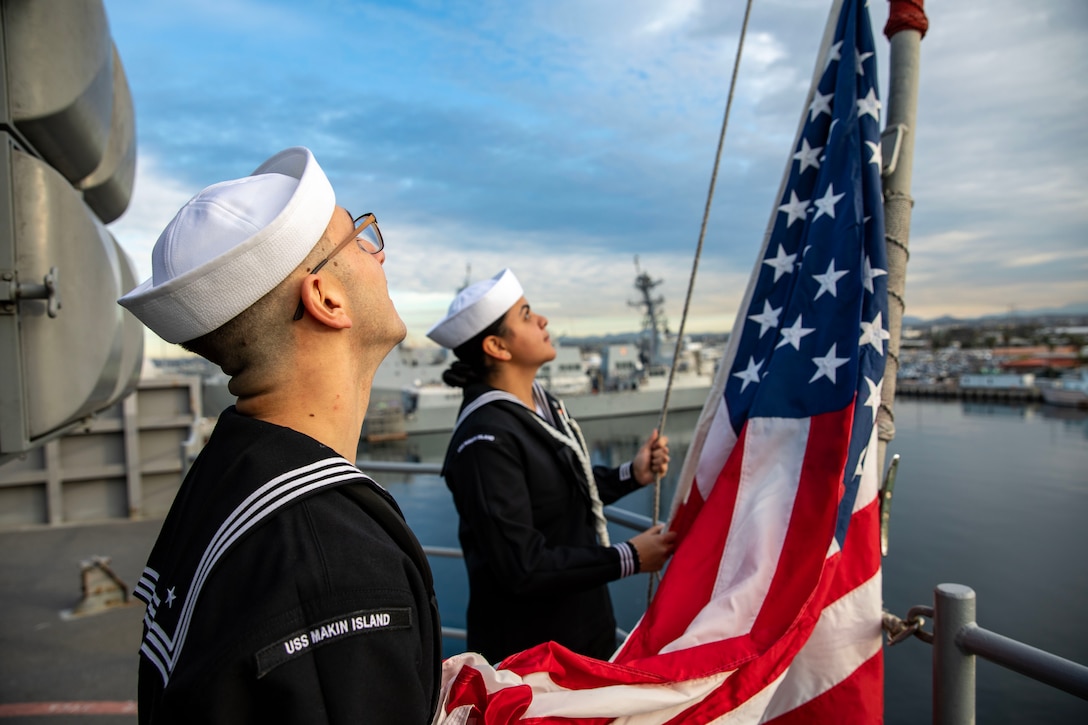 Two sailors look up at the U.S. flag on board a ship.