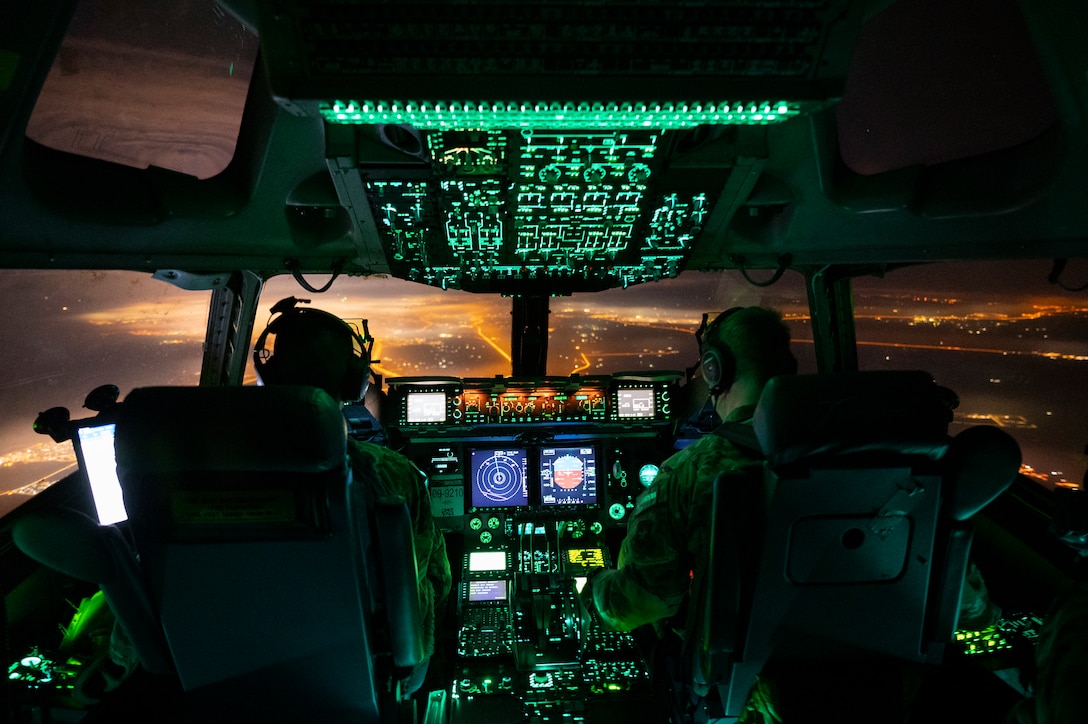 Two airmen operate an aircraft illuminated by control panels.