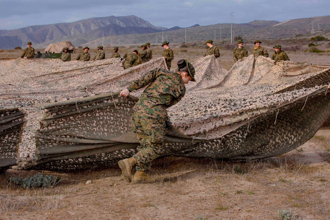 Sailors drag a camouflage netting.