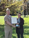 A civilian woman hold a certificate awarded to her from a Navy captain.