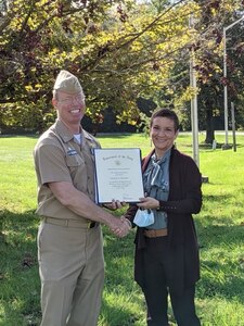 A civilian woman hold a certificate awarded to her from a Navy captain.