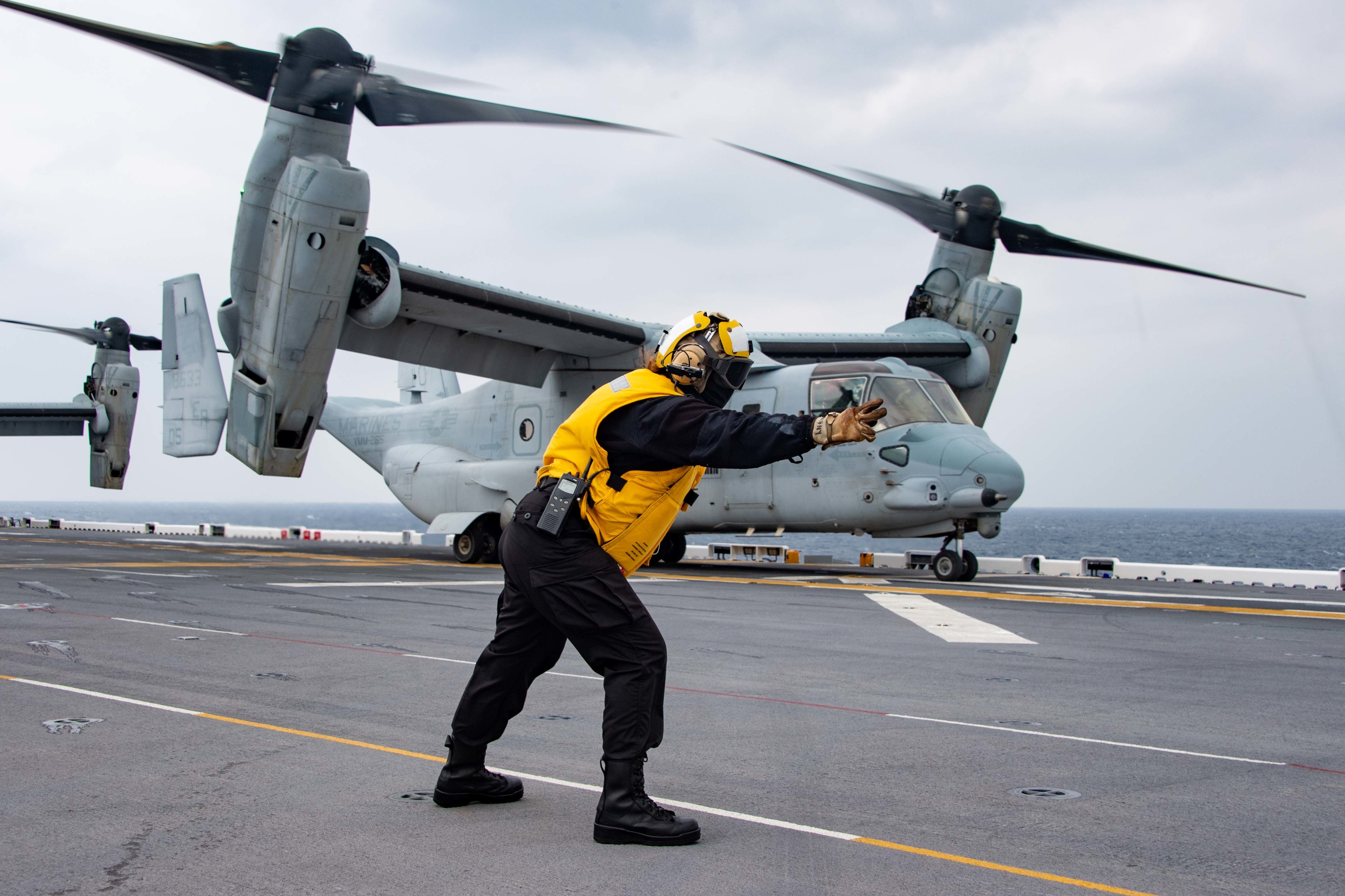 A Sailor assigned to the forward-deployed amphibious assault ship USS America (LHA 6), directs an MV-22B Osprey tiltrotor aircraft to launch from the ship's flight deck.