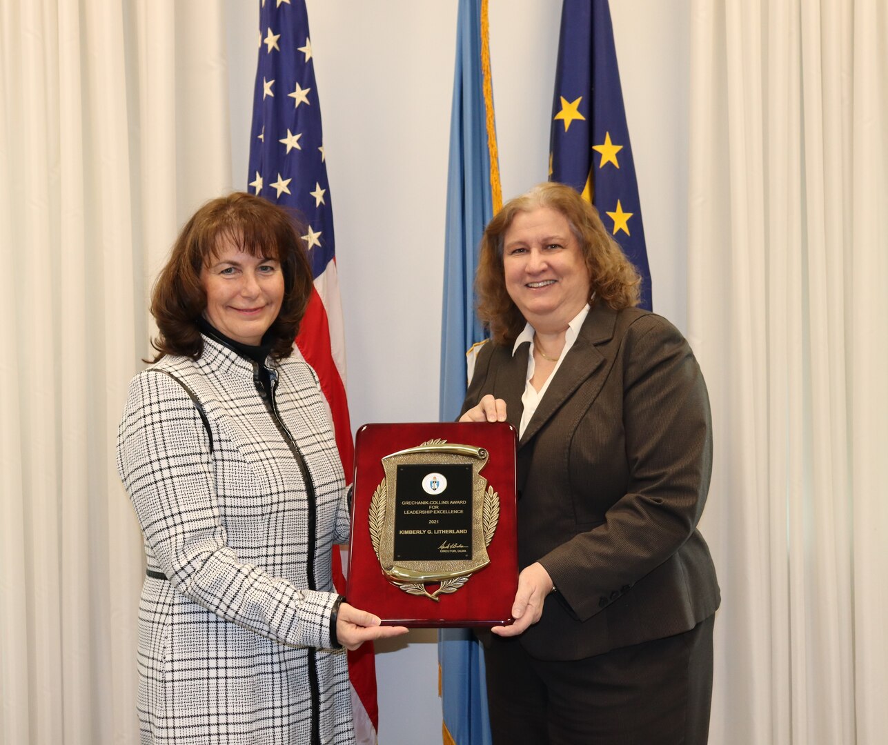 two women standing with an award and flags in the background