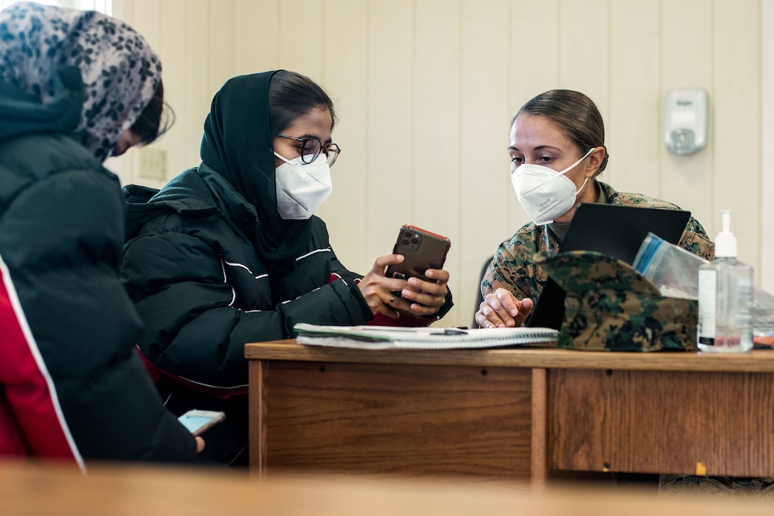 A Marine, wearing a face mask, assists an Afghan evacuee with creating a resume.