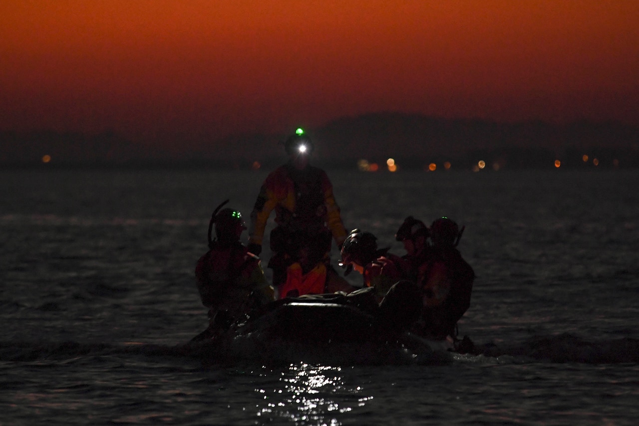 Airmen put a small boat together in a body of water in the dark.