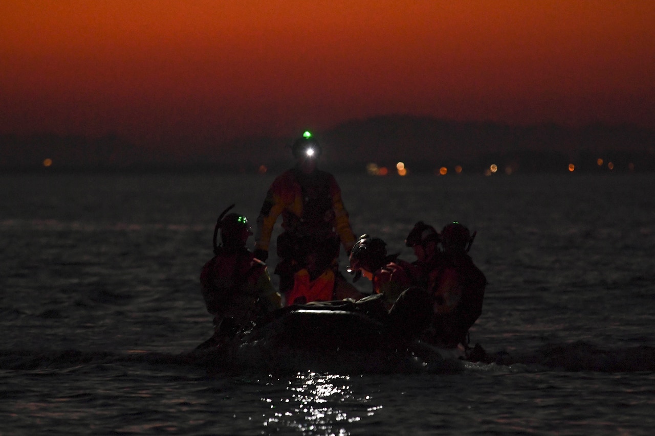 Airmen put a small boat together in a body of water in the dark.