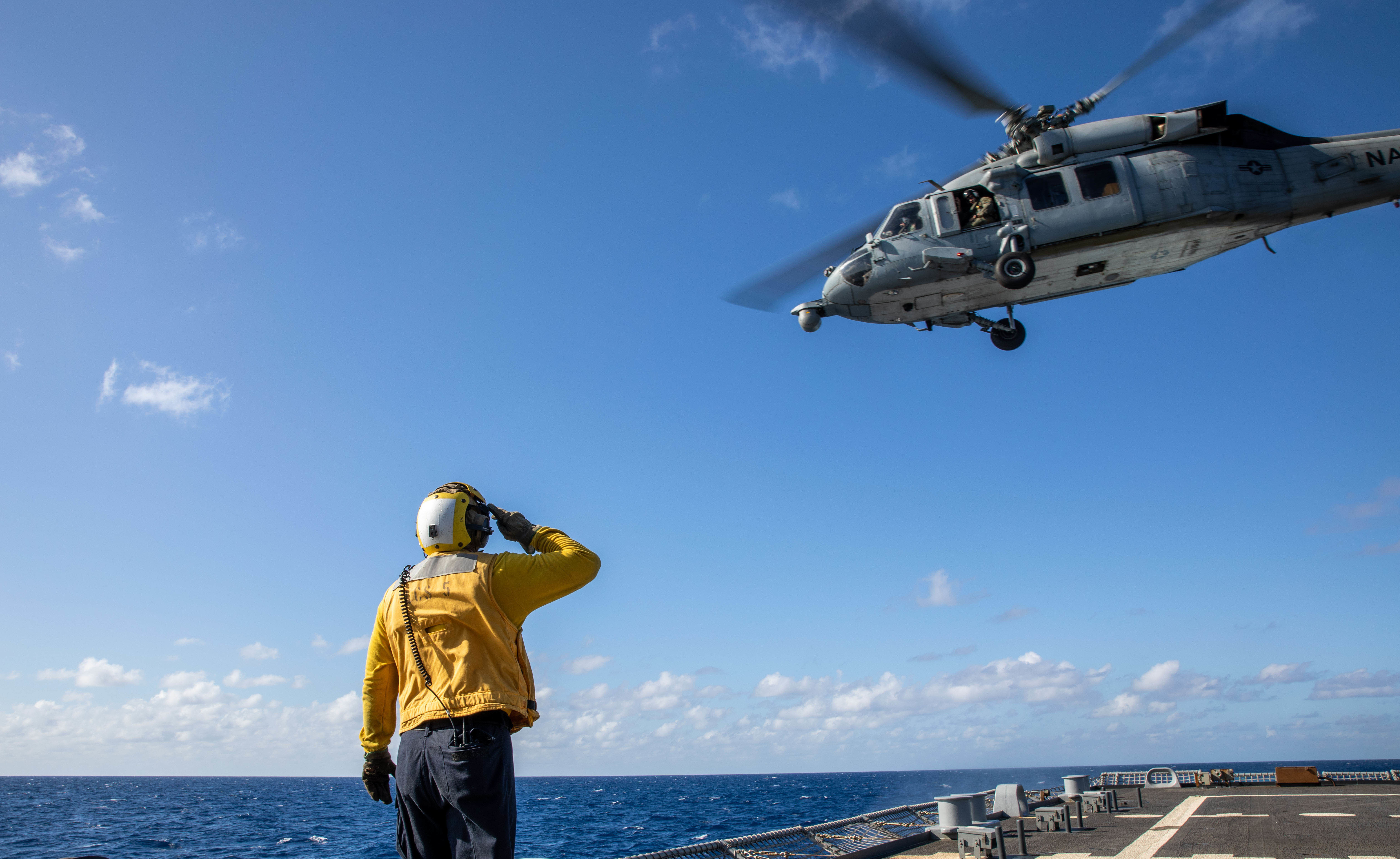 Boatswain’s Mate 2nd Class James Dowdee salutes the pilots in an MH-60S Sea Hawk helicopter assigned to the “Sea Knights” of Helicopter Sea Combat Squadron (HSC) 22, Detachment 5, as it flies above the Freedom-variant littoral combat ship USS Milwaukee (LCS 5).