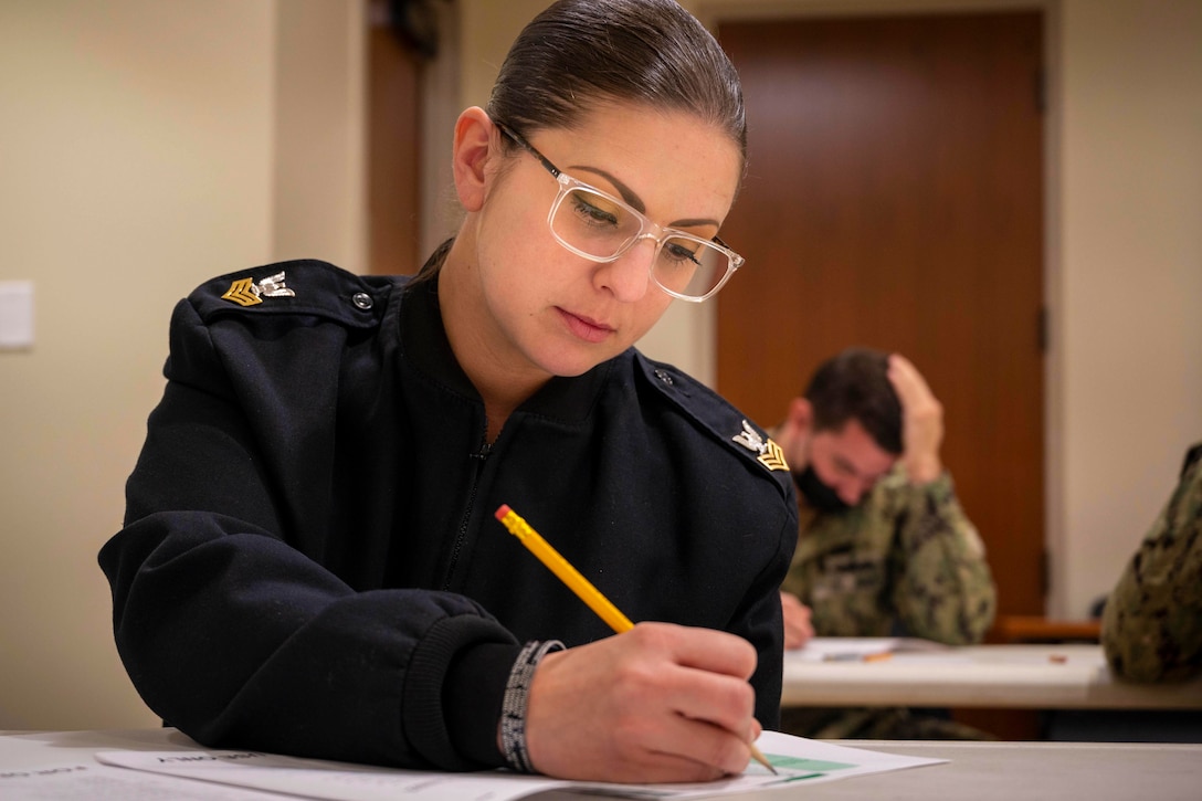 A sailor sits at a desk writing on a piece of paper.