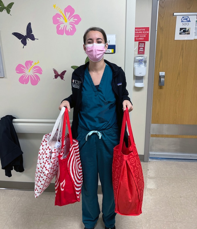 A woman in a medical uniform holds up bags of supplies.