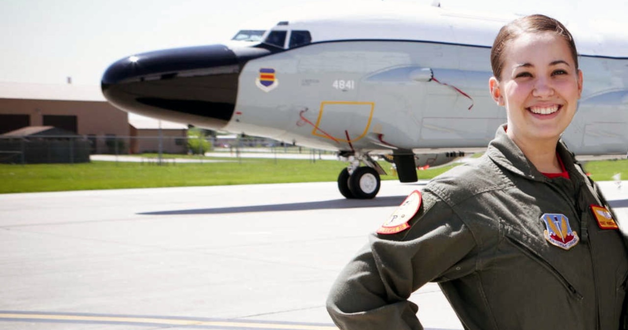 A woman in military uniform stands in front of a military aircraft.