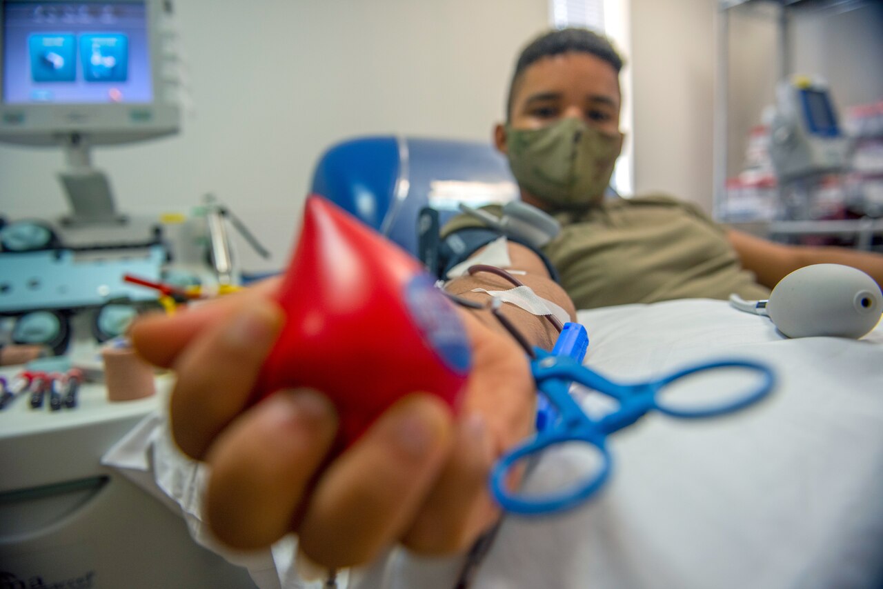 A man in military uniform holds a stress ball while donating blood.