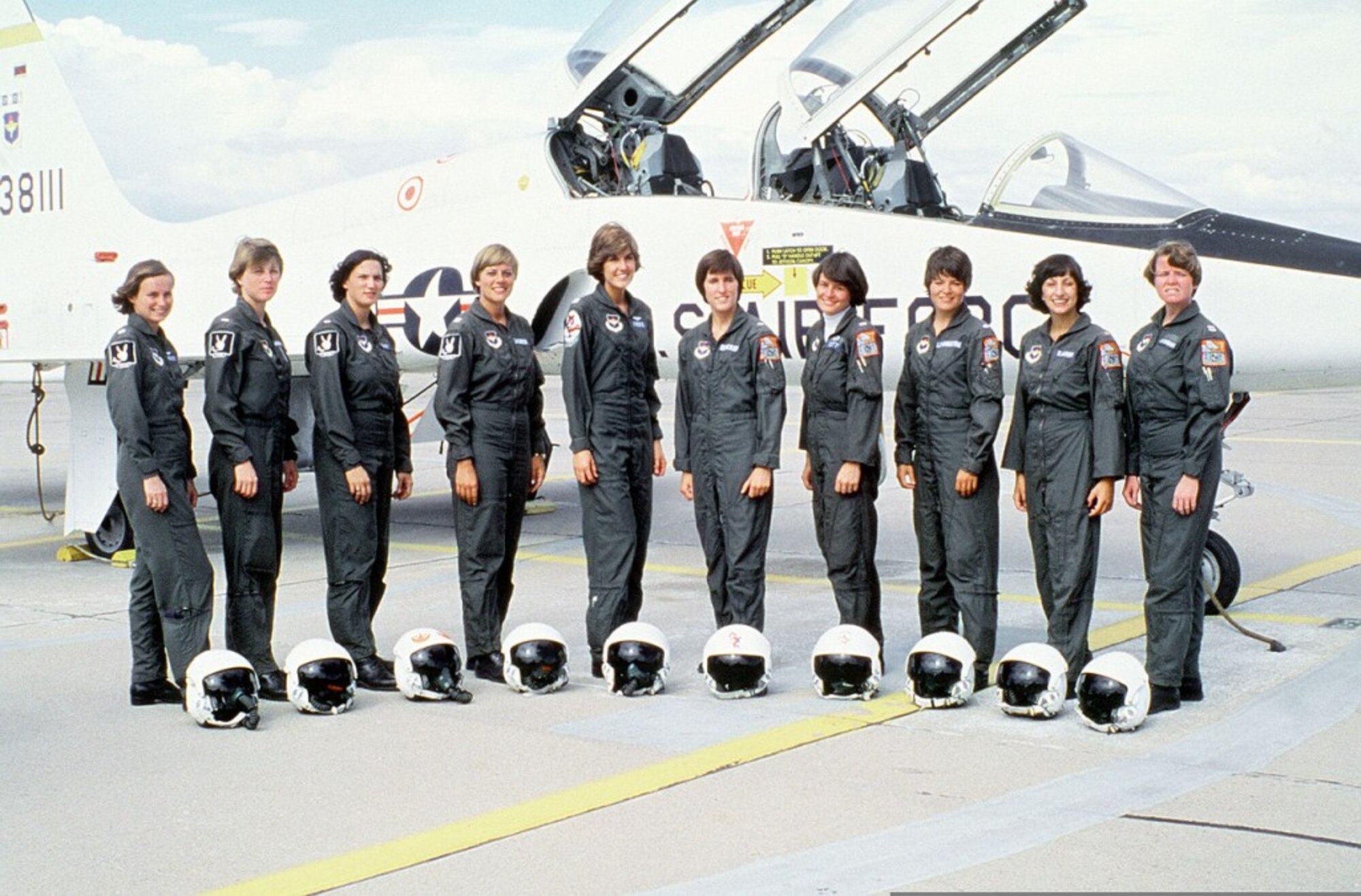 ten women dressed in flight gear stand in front of a aircraft