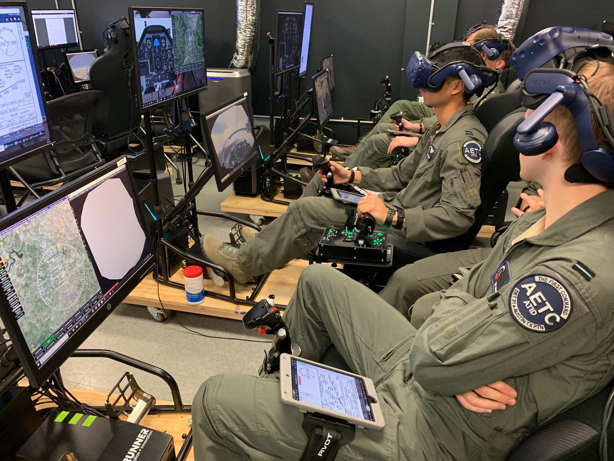 Royal Air Force Flight Officer Syd Janota (fore), Pilot Training Next 2.0 student, observes a fellow student flying a virtual-reality training sortie at the PTN facility at the Armed Forces Reserve Center