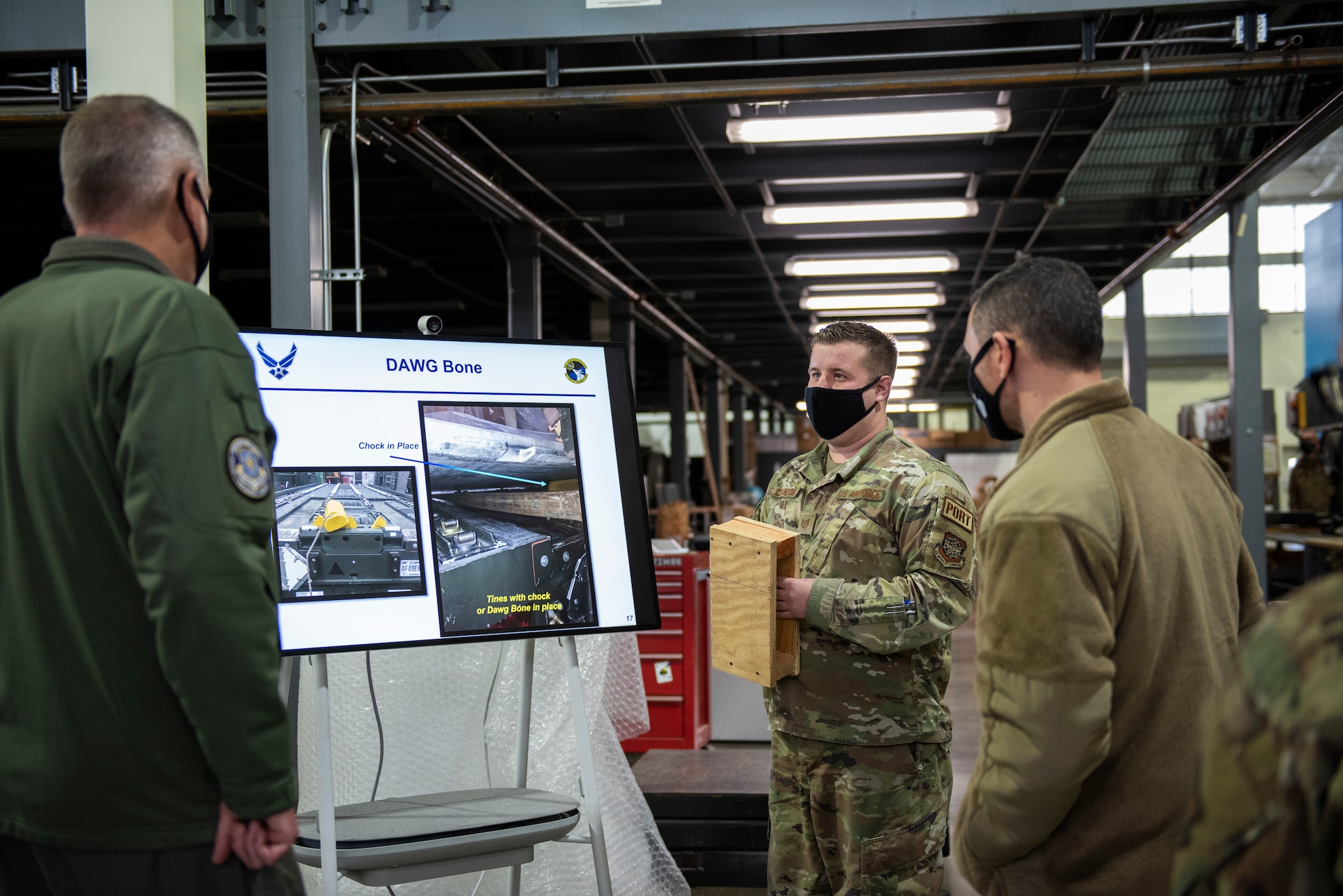 Tech. Sgt. Daniel Clanton (middle), 92nd Logistics Readiness Squadron non-commissioned officer-in-charge of Air Transportation Function, showcases an innovative tool to Gen. Mike Minihan, Air Mobility Command commander (left), and Chief Master Sgt. Brian Kruzelnick, AMC command chief (right), during a base tour at Fairchild Air Force Base, Washington, Jan. 6, 2022. Clanton explained the safety benefits of the ‘DAWG Bone’ tool to the AMC Command Team. (U.S. Air Force photo by Amn Jenna A. Bond)