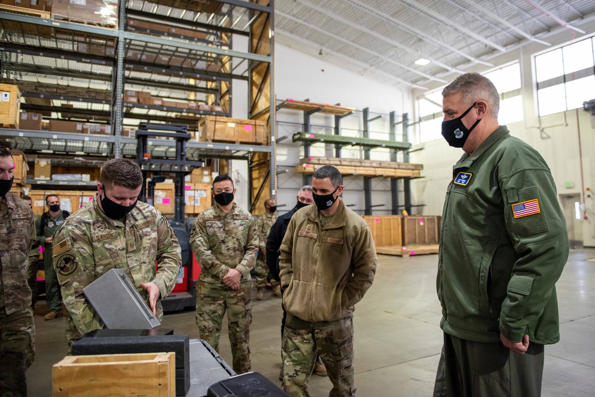 Tech. Sgt. Daniel Clanton (front left), 92nd Logistics Readiness Squadron non-commissioned officer-in-charge of Air Transportation Function, showcases an innovative tool to Gen. Mike Minihan, Air Mobility Command commander (right), and Chief Master Sgt. Brian Kruzelnick, AMC command chief (middle), during a base tour at Fairchild Air Force Base, Washington, Jan. 6, 2022. Clanton explained the safety benefits of the ‘DAWG Bone’ tool to the AMC Command Team. (U.S. Air Force photo by Amn Jenna A. Bond)