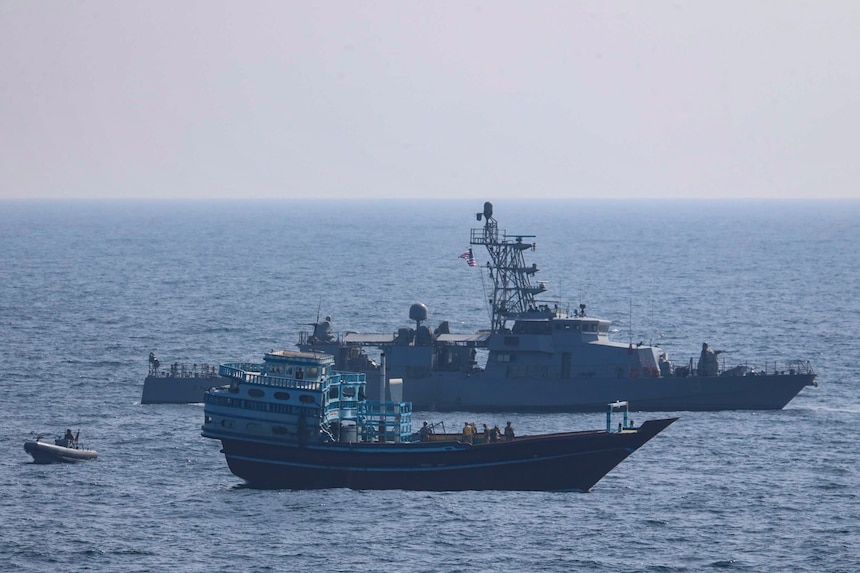 U.S. service members conduct a boarding on a stateless fishing vessel transiting international waters in the Gulf of Oman as a rigid-hull inflatable boat and patrol coastal ship USS Chinook (PC 9) station nearby.