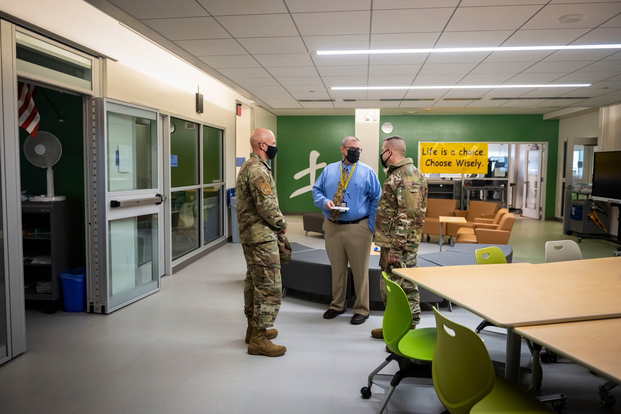 Two men in military uniform talk to school staff member in a hallway.