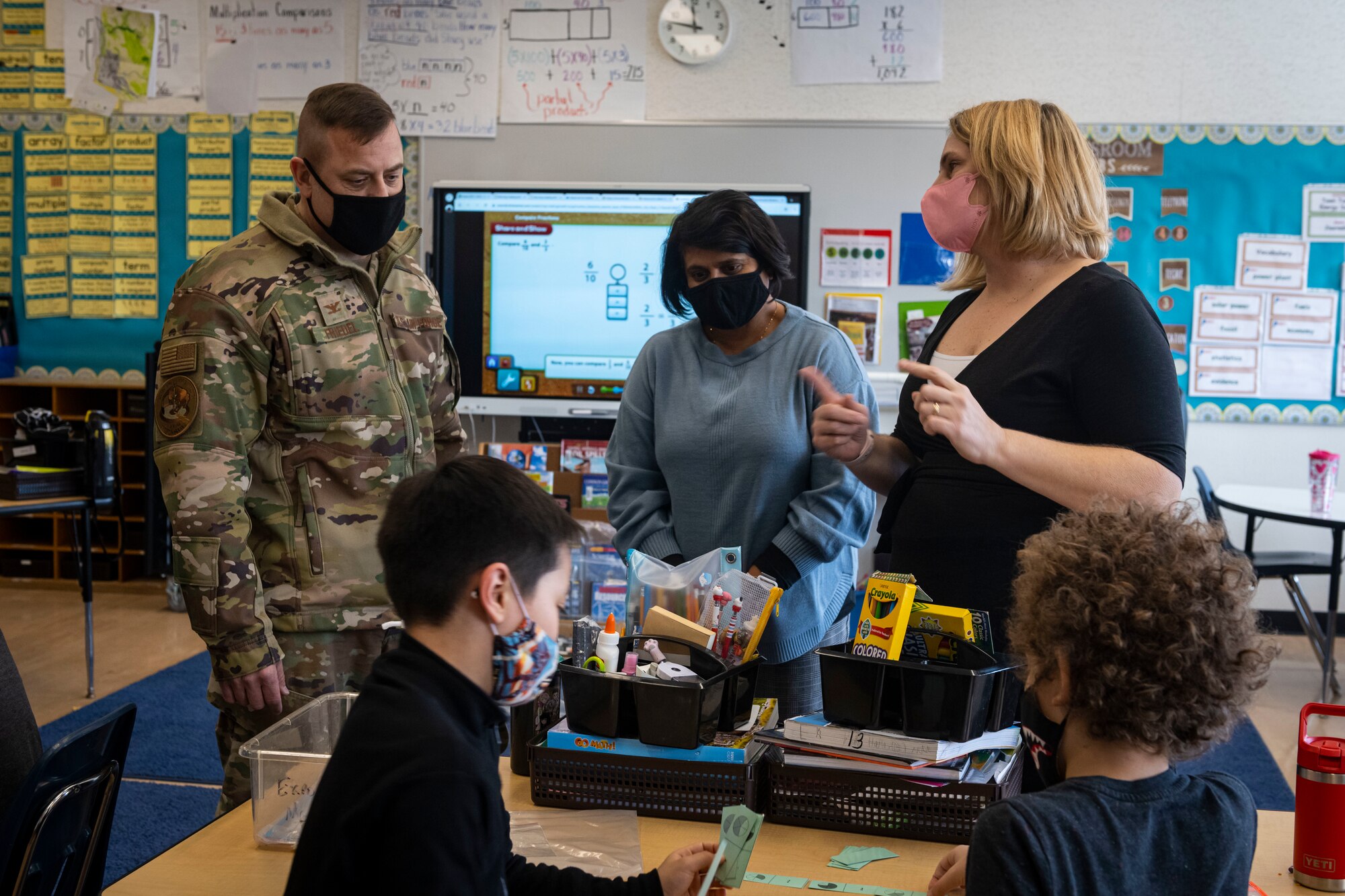 Man in military uniform talk to two school staff members in a classroom.