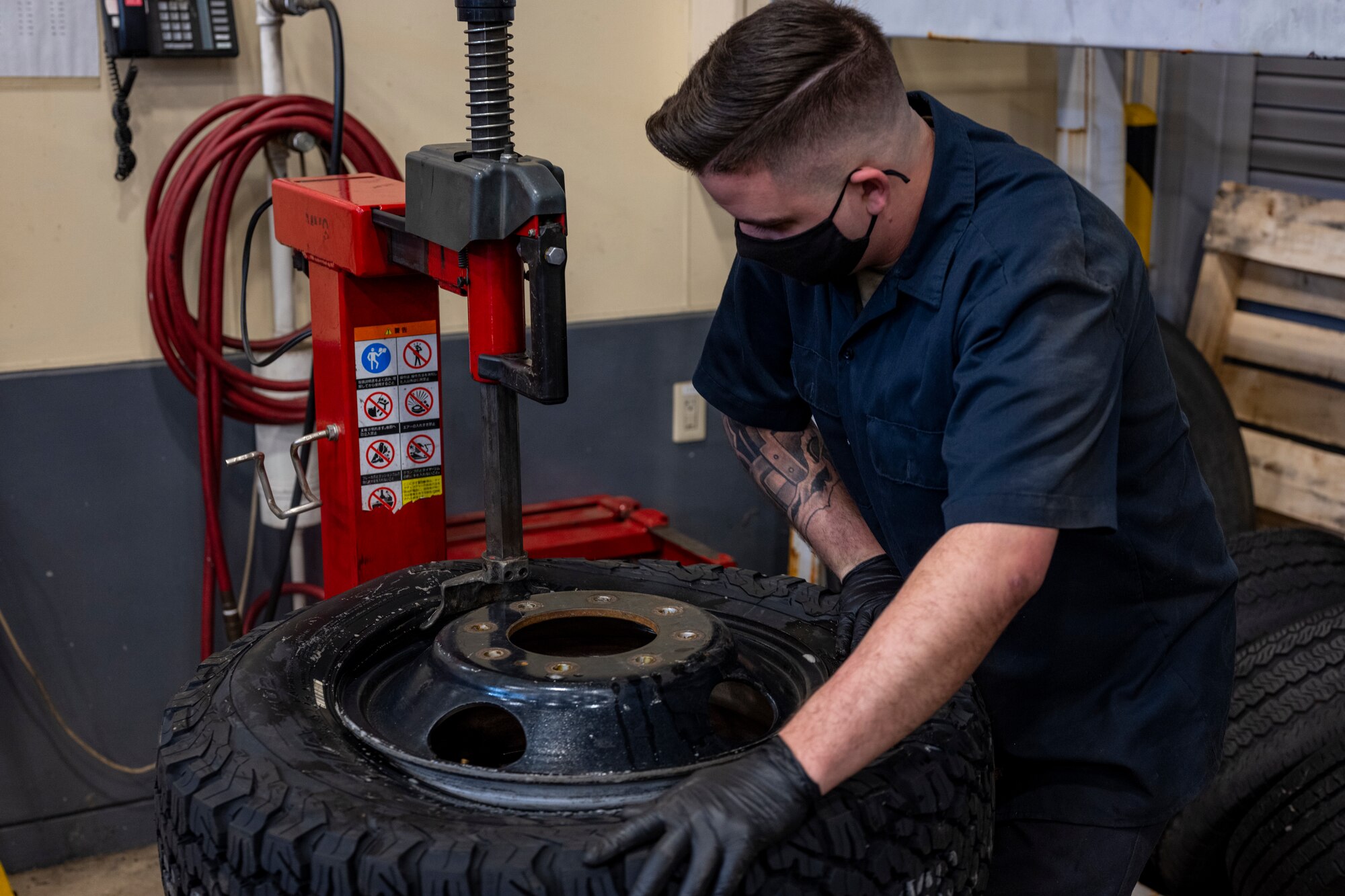 Airman putting tire onto a rim using heavy machinery.