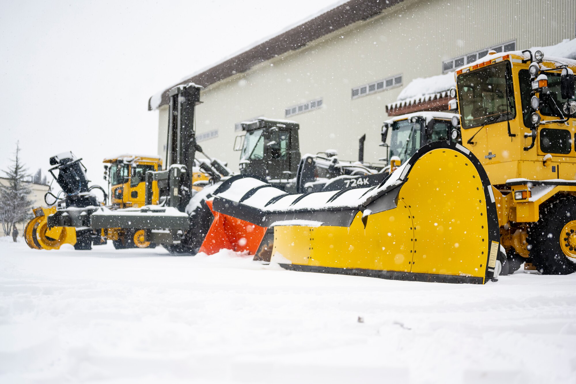 Heavy snow plow machinery sitting outside of garages.