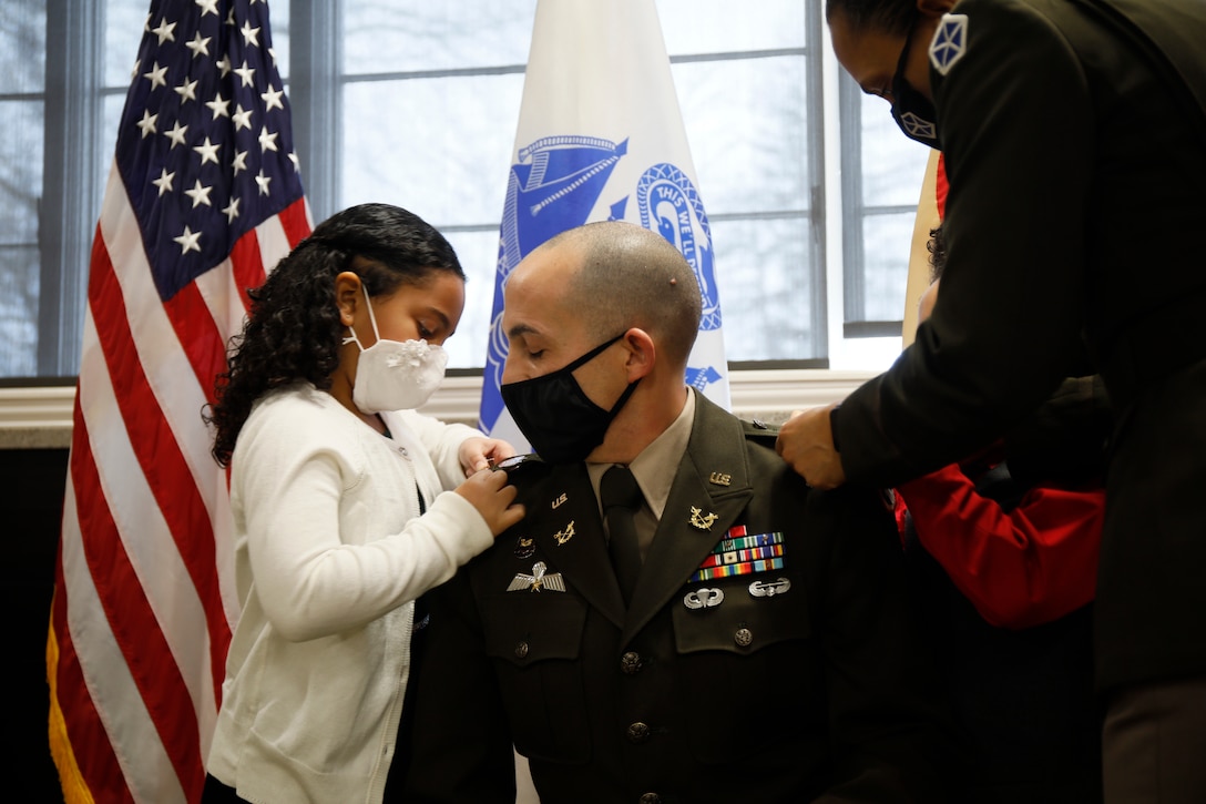 A young girl pins a rank on a man's uniform.