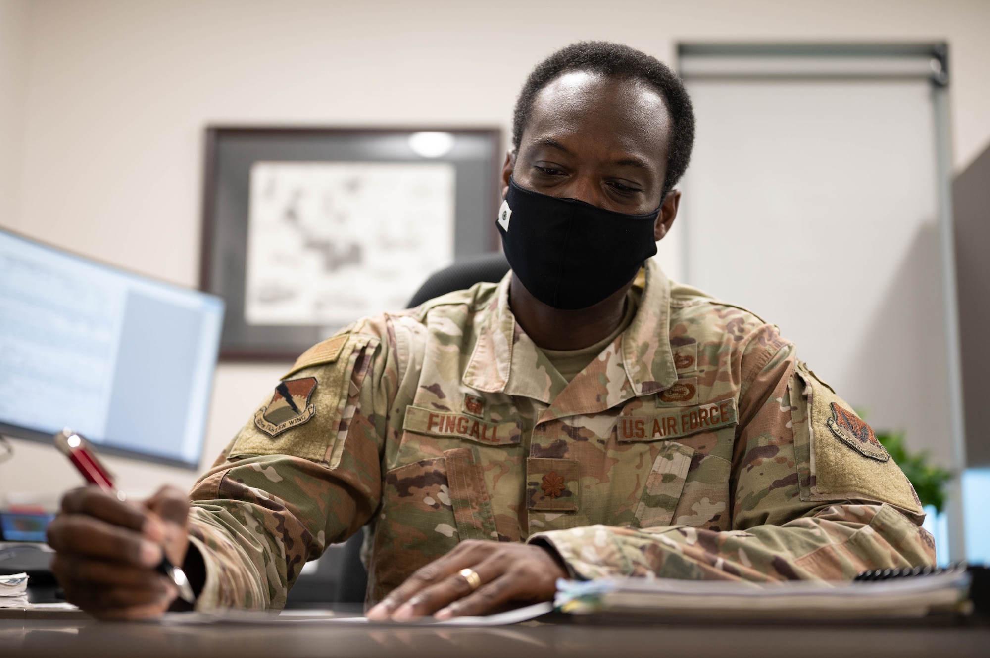 A uniformed man holds a pen as he sits at his desk looking at paperwork.