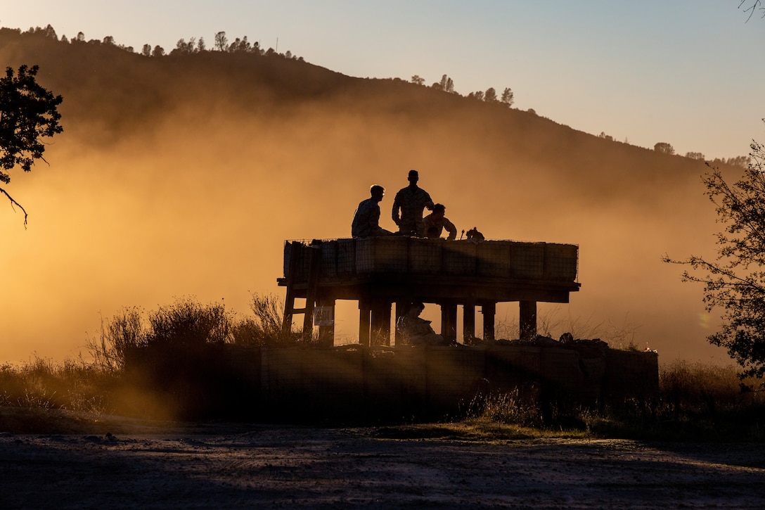 Marines stand together in a small structure with dust around them.