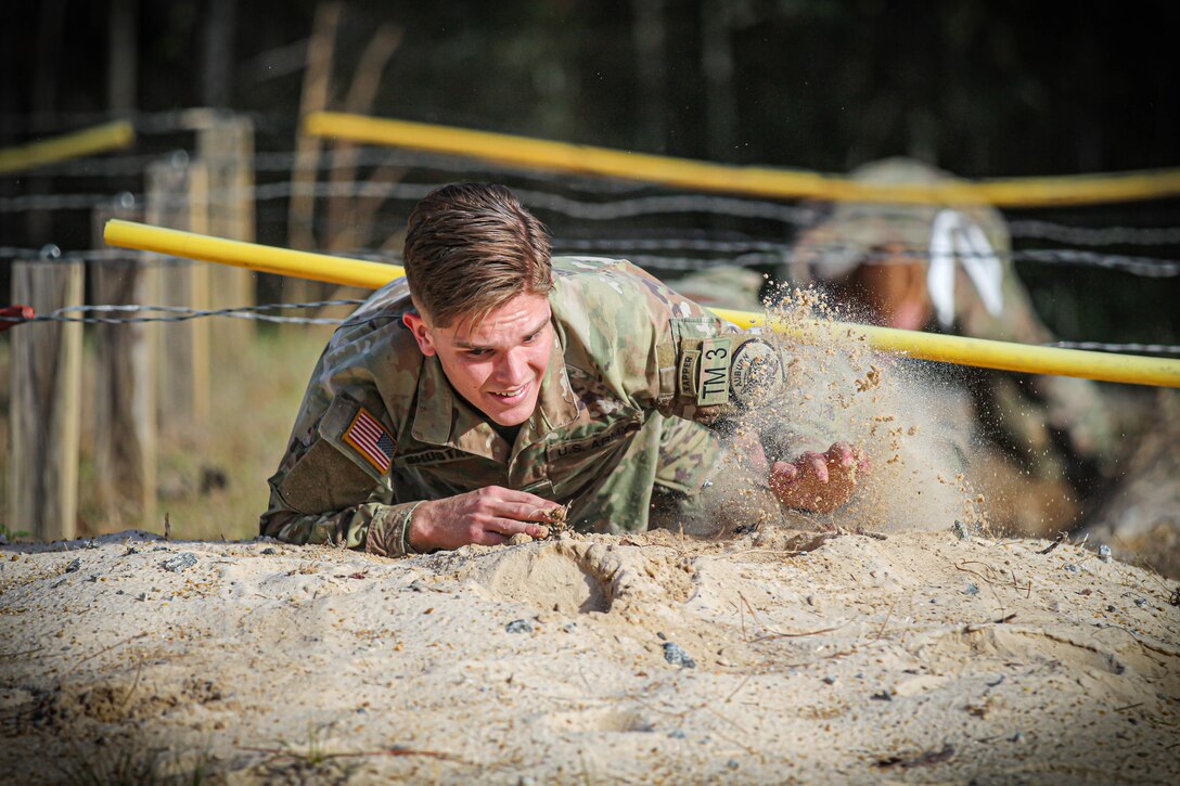 A cadet crawls in the sand underneath wires.