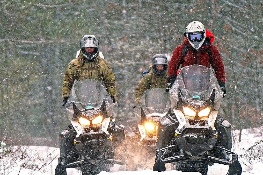 Three soldiers ride on snowmobiles as snow falls.