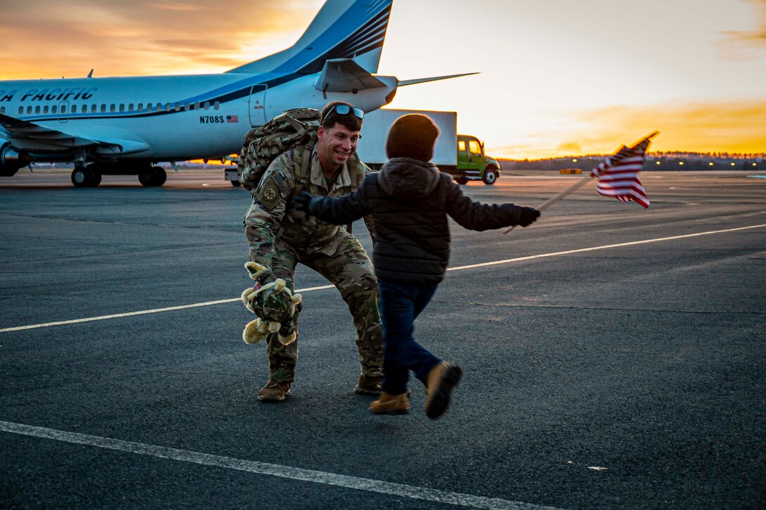 A soldier crouches to hug a child.