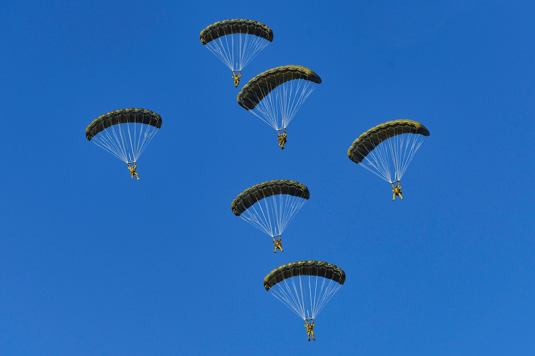 Six airmen descend in the sky wearing parachutes.