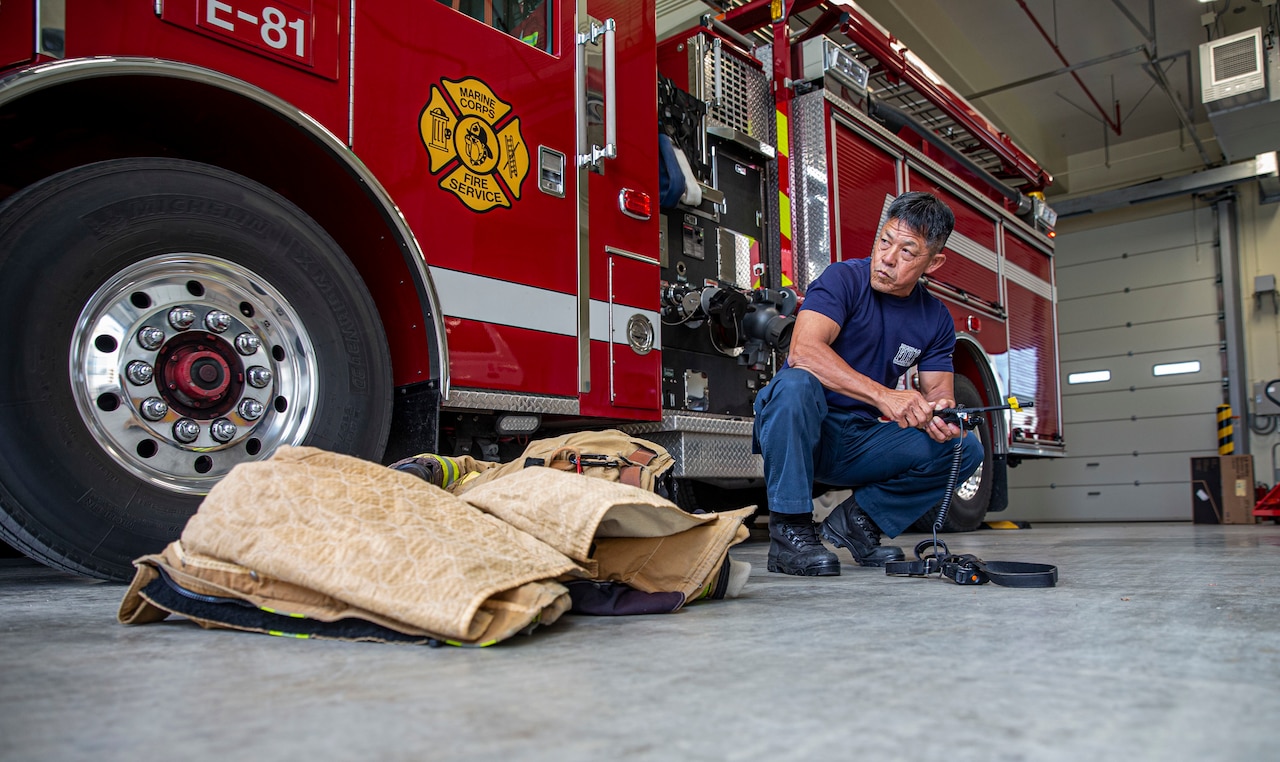 A firefighter kneels by a firetruck in a garage.