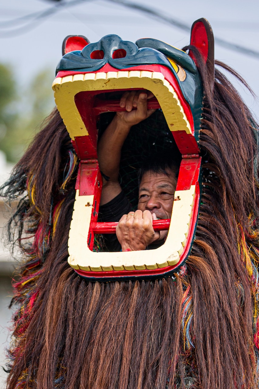 A man's face is visible inside a lion costume he's wearing.