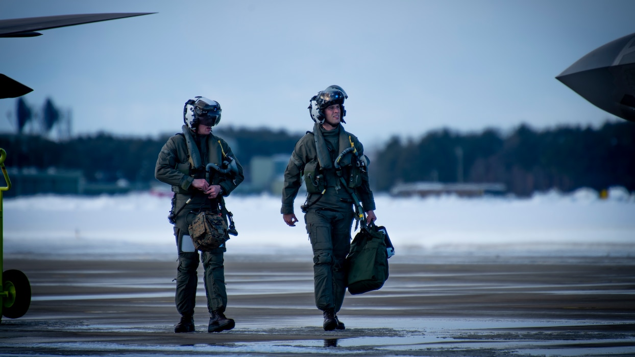 Two Men walk on a flightline wearing helmets