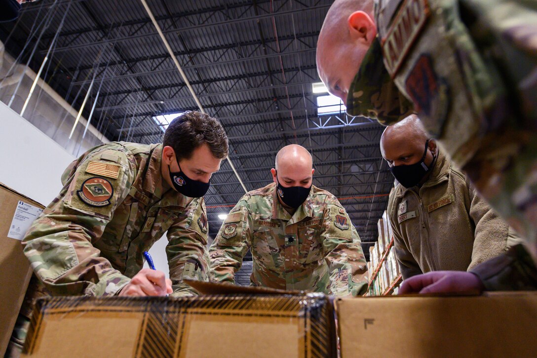 Four airmen wearing face masks lean over some large boxes.