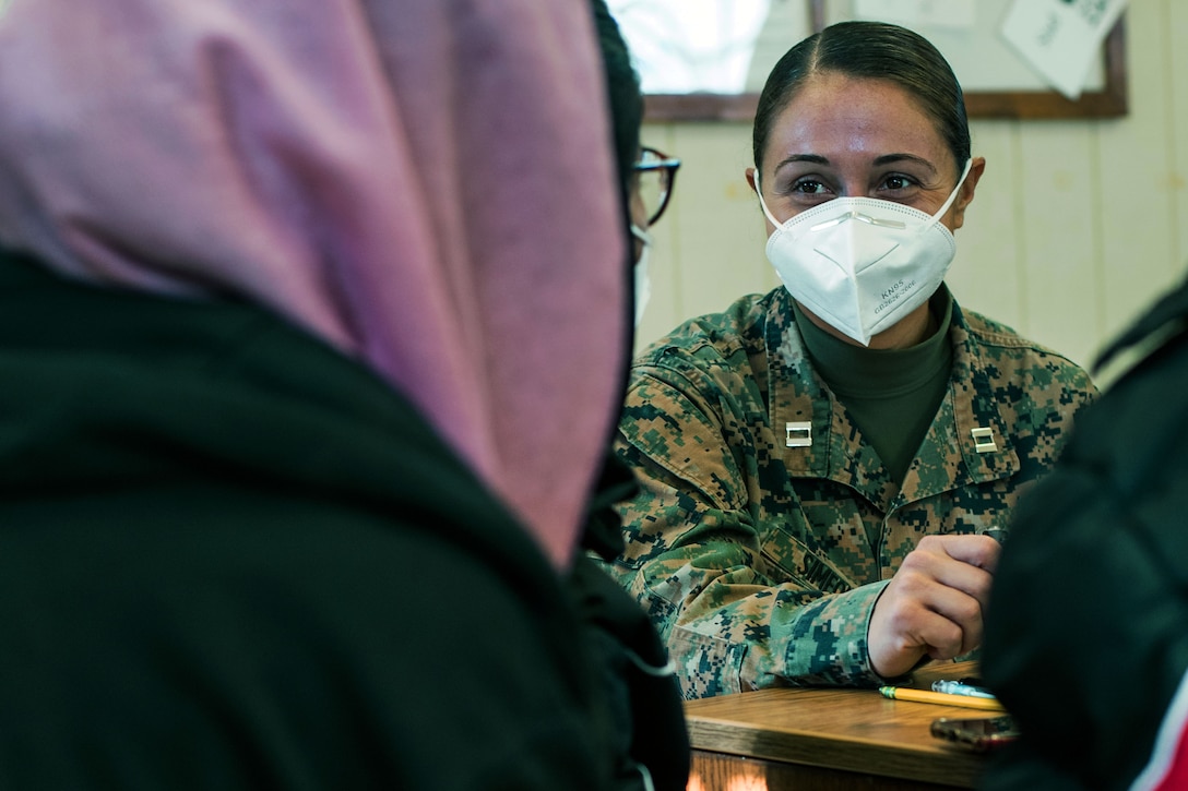 A Marine wearing a face mask assists an Afghan evacuee.