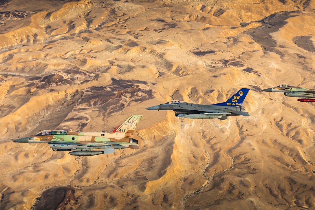 Military jets fly together above a desert landscape.