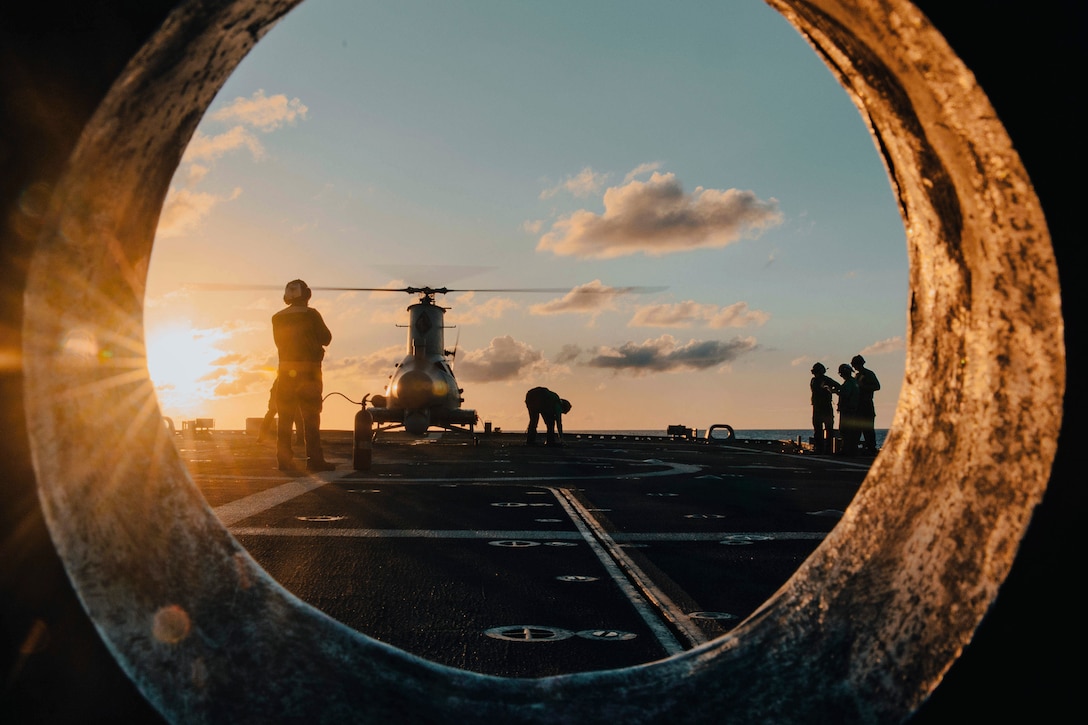 Sailors work on an unmanned aerial vehicle aboard a ship at sea under a sunlit sky.