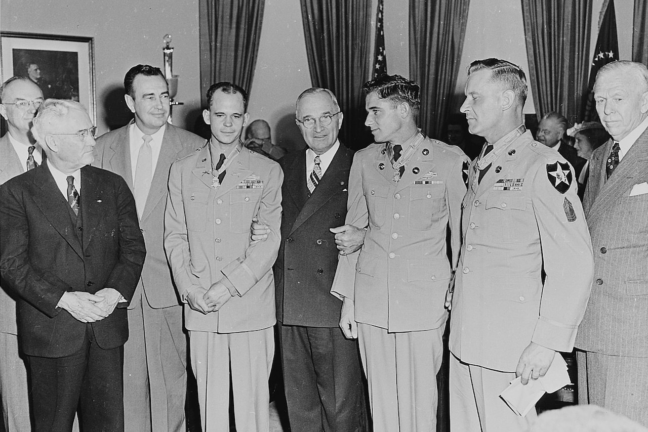 Eight men stand together for a photo. The man in the middle has his arms interlaced with the two men besides him.