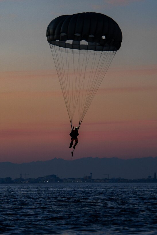 An airman freefalls with a parachute over a body of water.