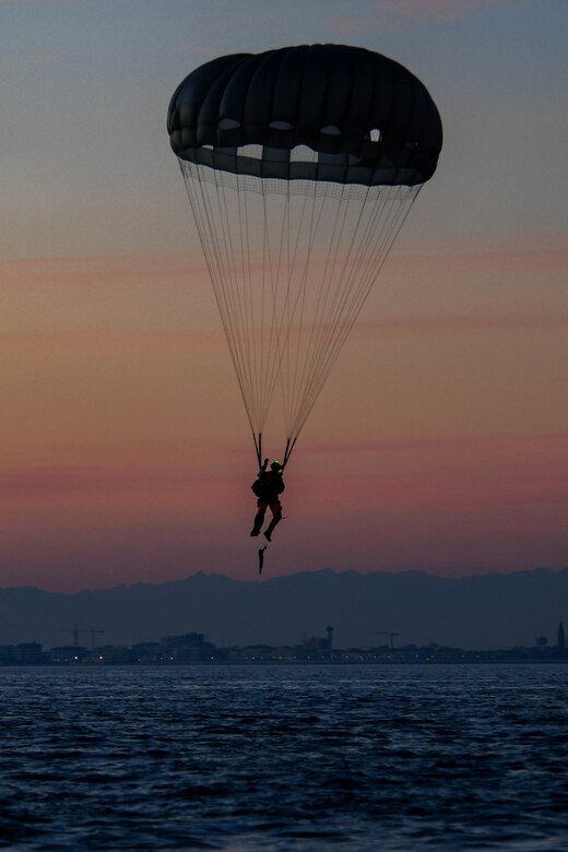 An airman freefalls with a parachute over a body of water.