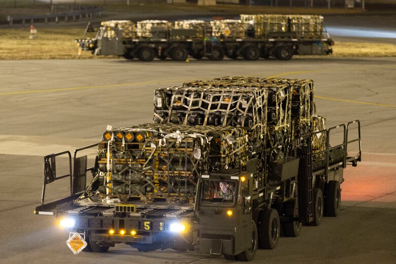 A utility vehicle moves across a large concrete surface and carries cargo pallets.