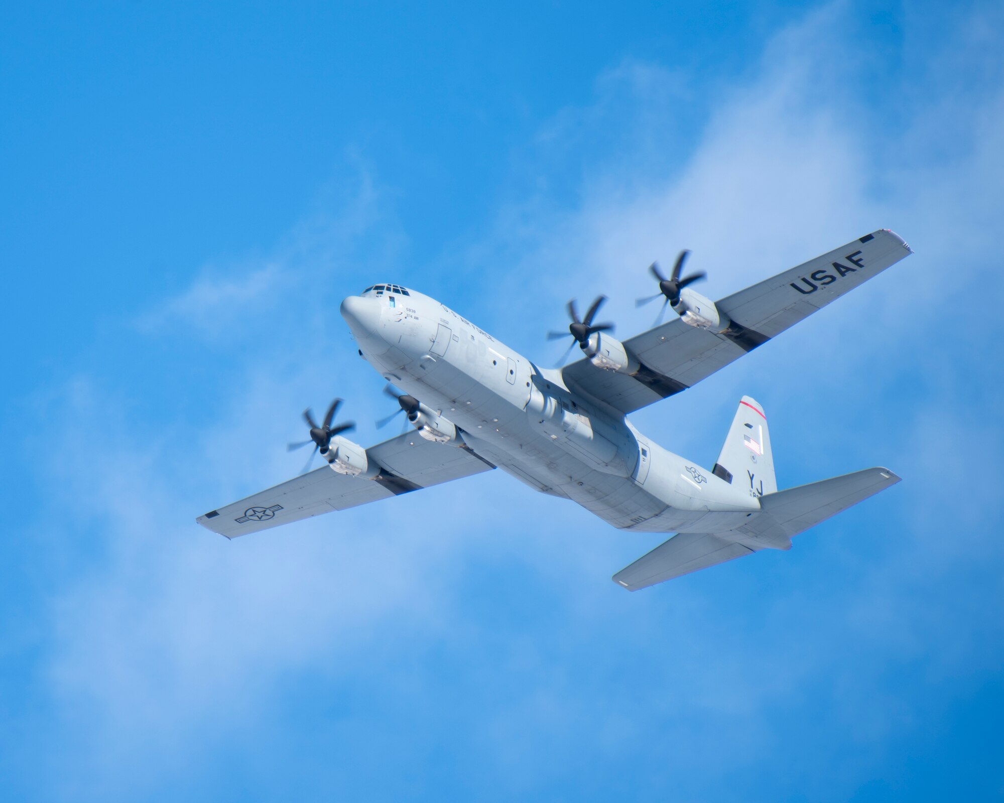 A a grey aircraft flies across a blue sky with a few clouds