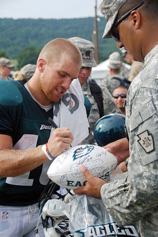 A football player signs an autograph for a service member.