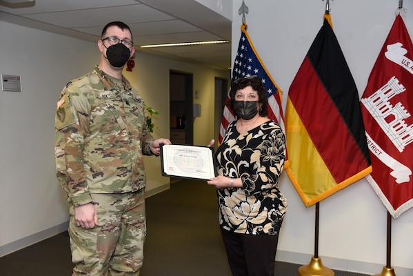 U.S. Army Lt. Col. Daniel J. Fox, deputy commander of the U.S. Army Corps of Engineers Europe District, presents Cheryl Young of the U.S. Army Corps of Engineers Transatlantic Middle East District, with a certificate during a recognition ceremony in Wiesbaden, Germany, Jan. 13, 2022. Ms. Young processed over 100 special issuance passport applications within a week for Europe District personnel and their family members. (U.S. Army photo by Alfredo Barraza)