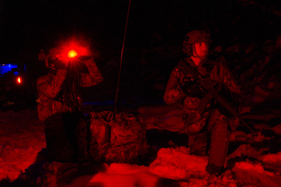 Two airmen illuminated by red light kneel in the snow.