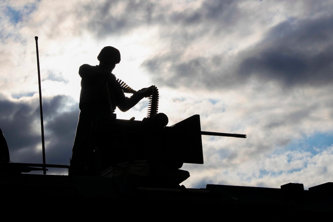 A Marine shown in silhouette reloads a gun.