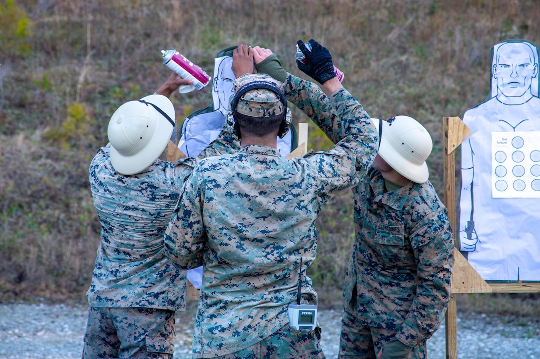 Three Marines glue a paper target onto its backing.