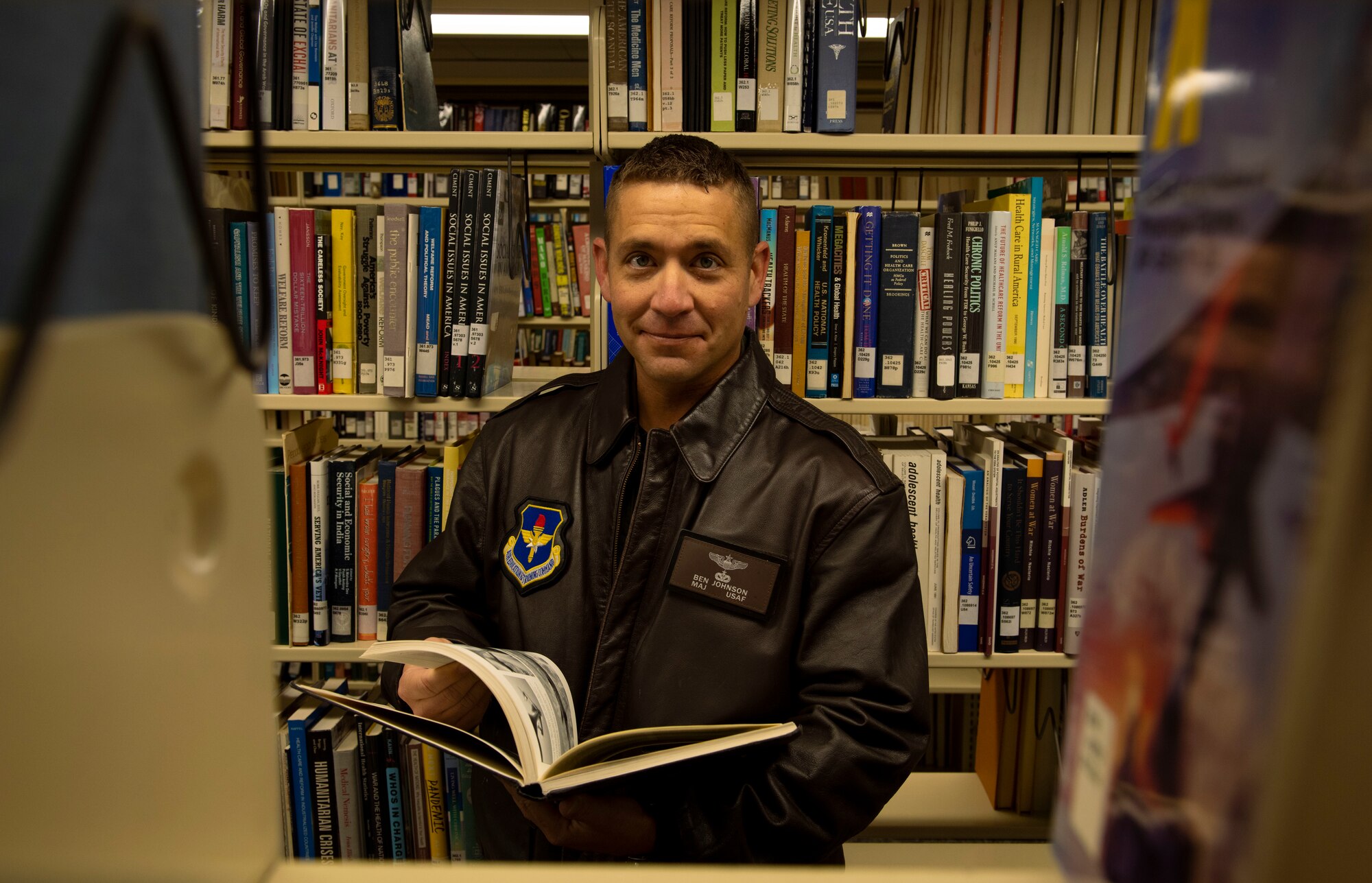 Maj. Benjamin Johnson is seen looking through a book while standing between shelves at the Air University Library.