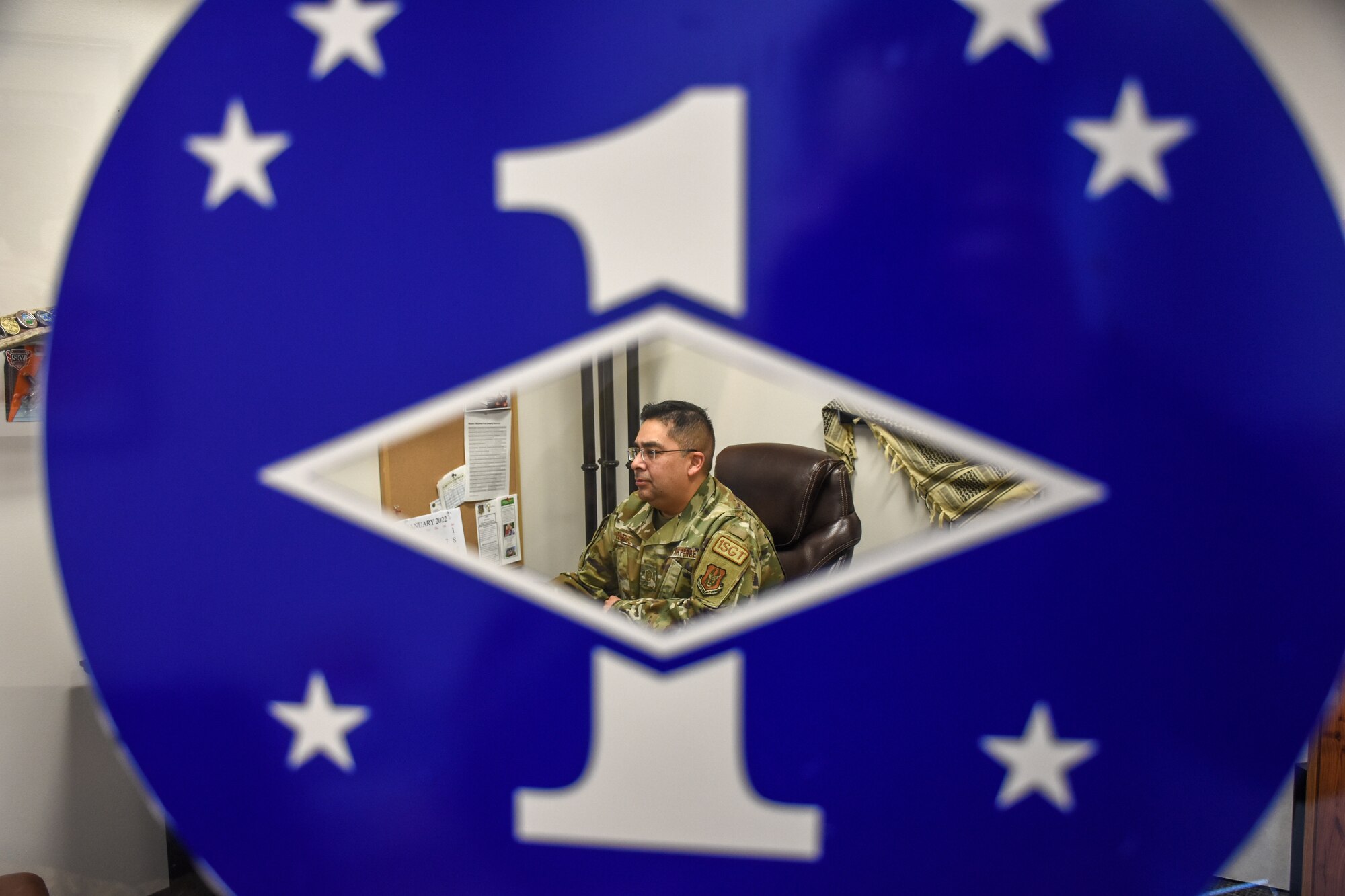 A man sits in a chair, facing left. Only his torso is visible through a diamond-shaped hole in a large blue sticker.